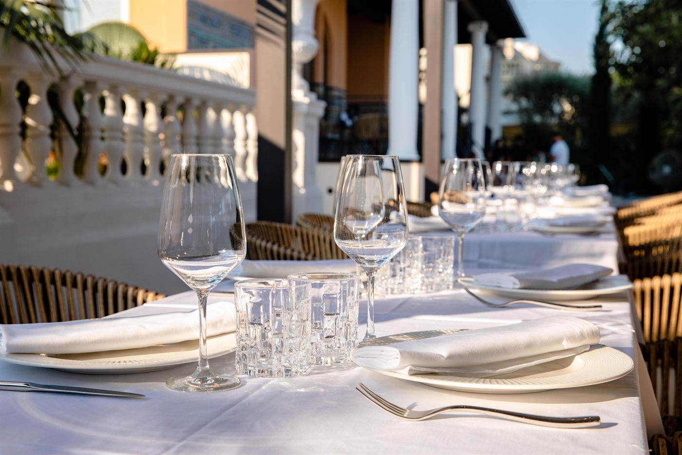 A long table laid with glassware and white linen on the restaurant terrace
